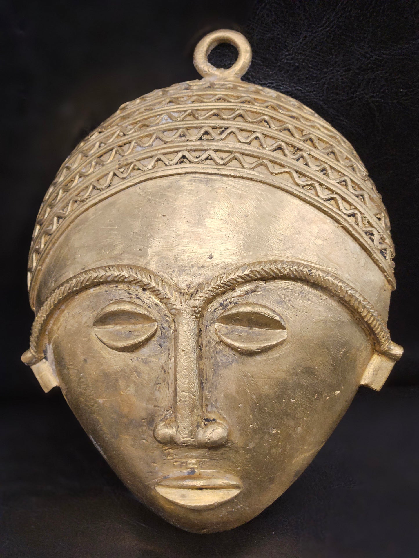 Close-up detail of Ghanaian handmade tribal brass mask, highlighting intricate etching and smooth finish