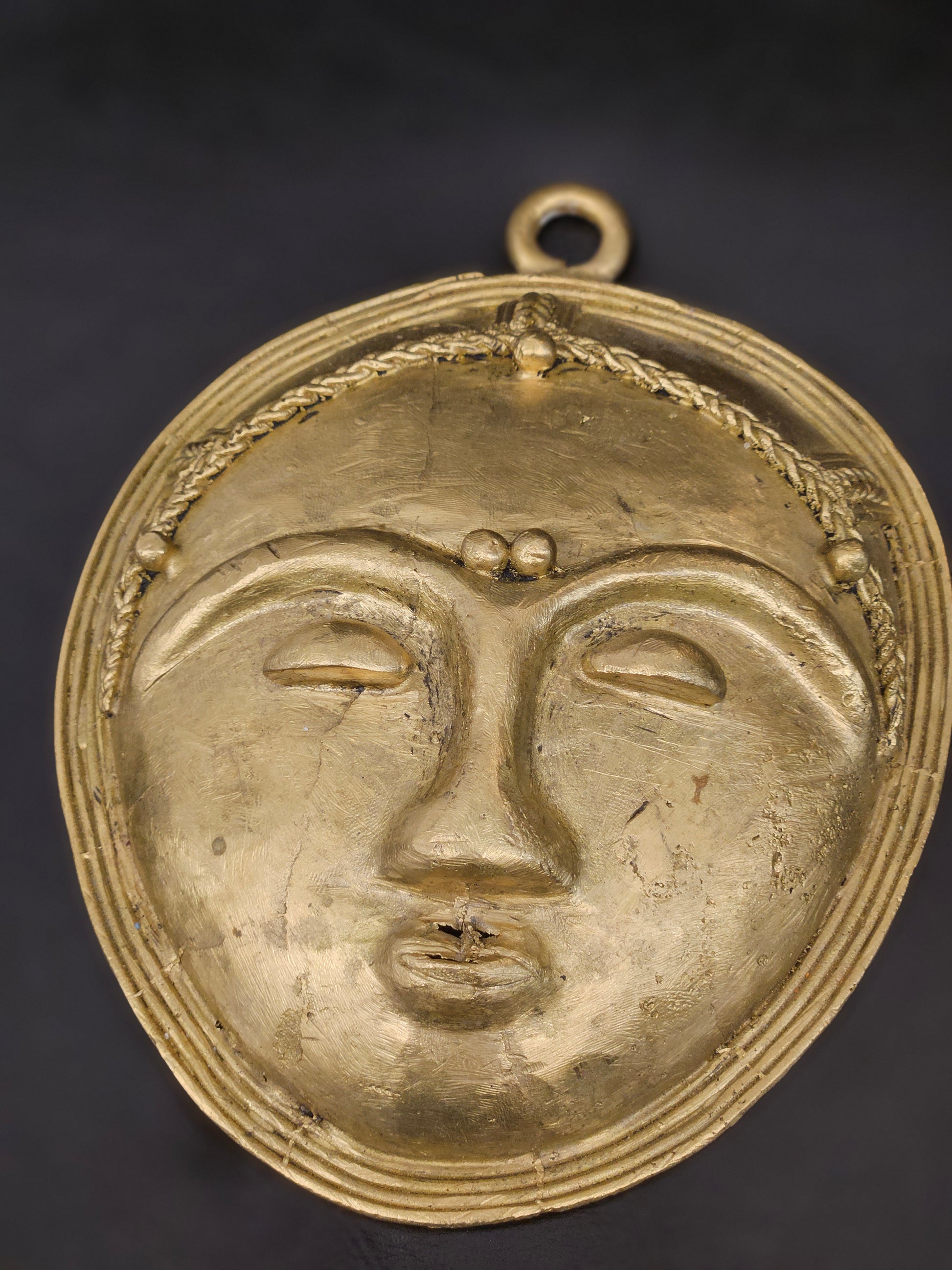 Back view of authentic African brass wall mask, showcasing ring for hanging and handmade detail