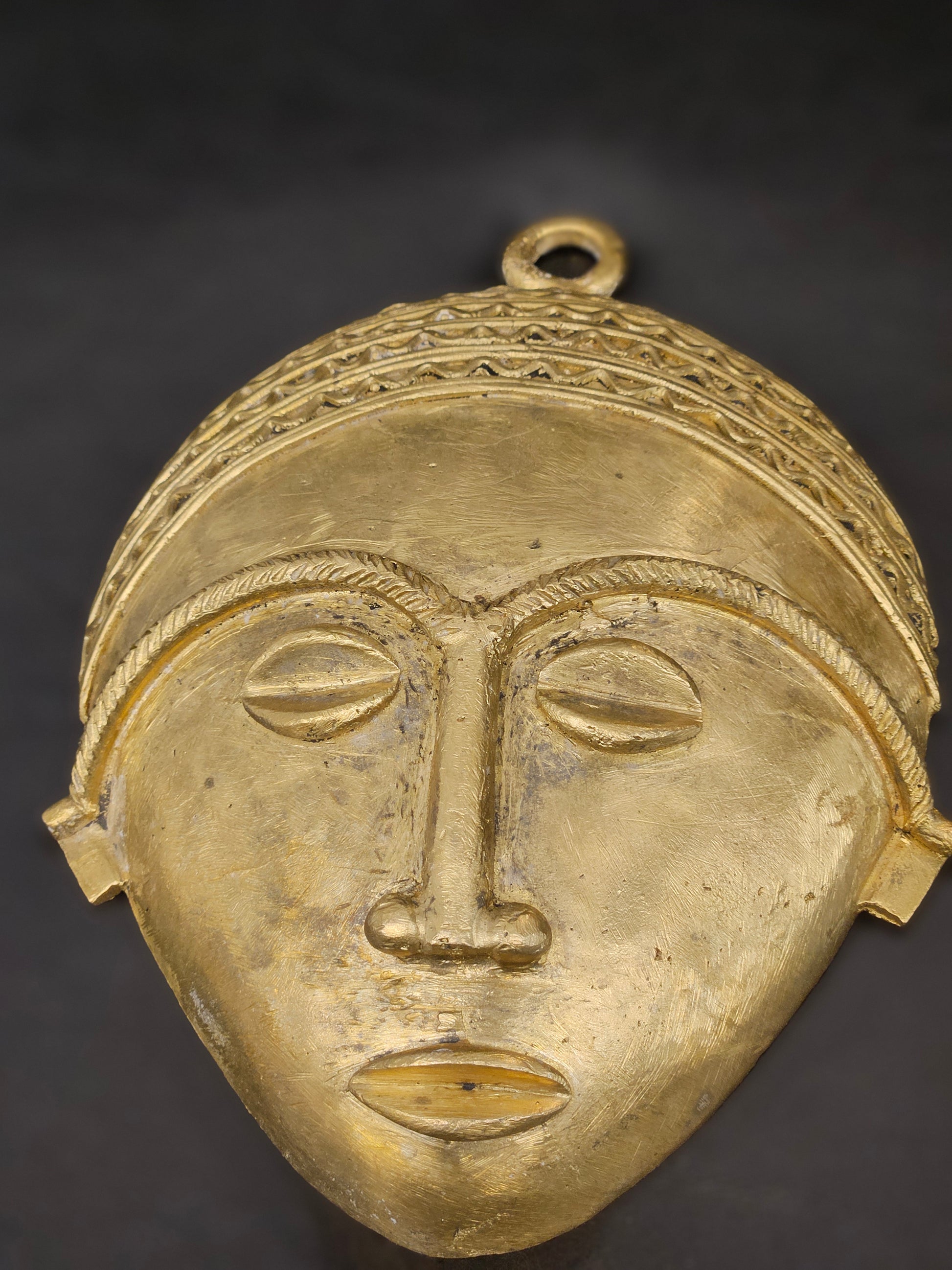 Zoomed-in shot of brass surface texture and facial detailing on African tribal mask, showing artisan craftsmanship