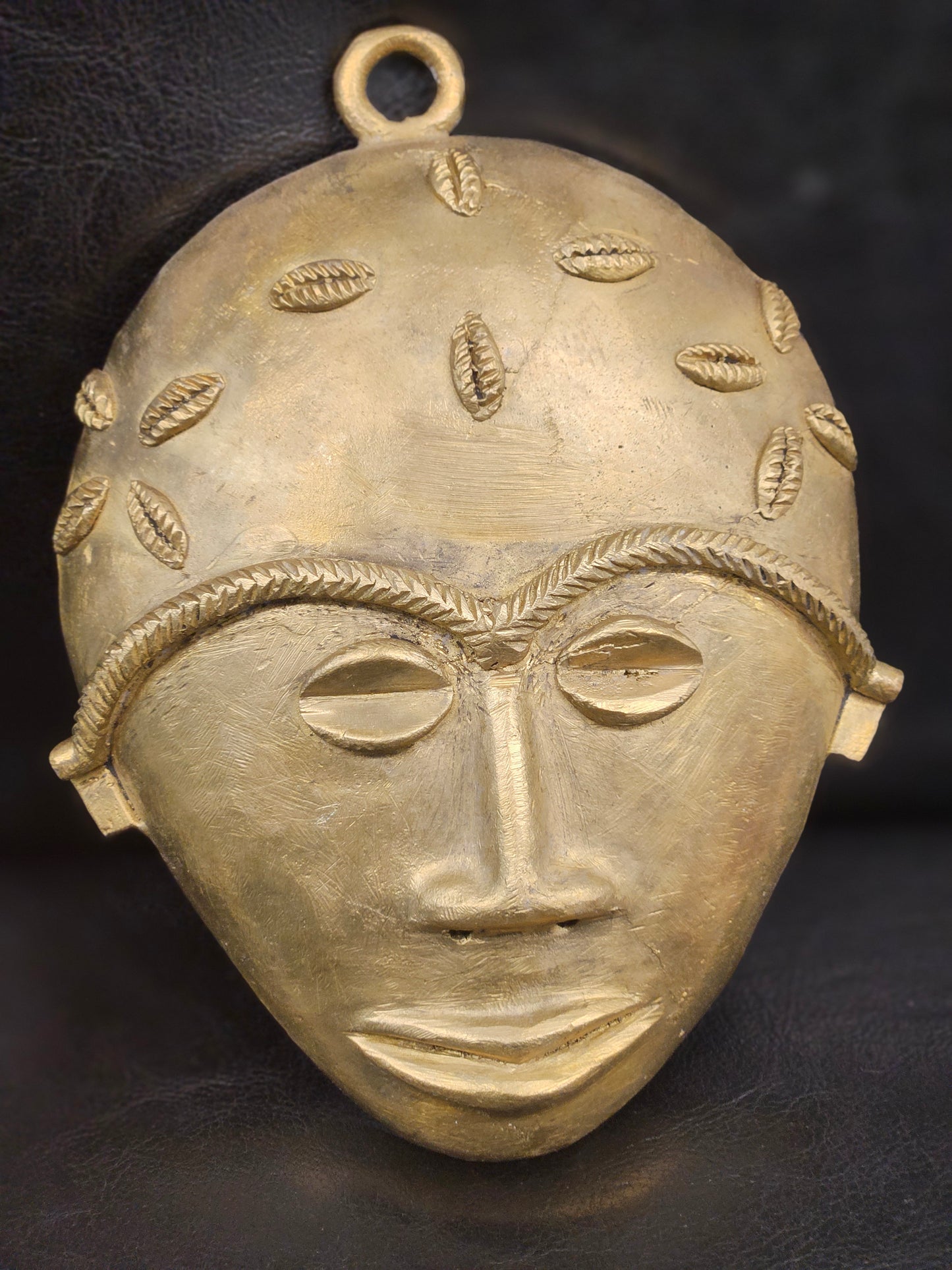 Close-up of cowrie-shell tribal engravings on an African brass mask handcrafted by Ashanti artisans in Ghana.